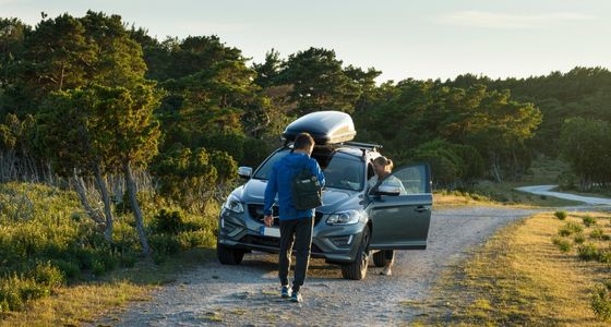 Et par st&aring;r ved en parkert bil med takboks langs en grusvei i naturen.