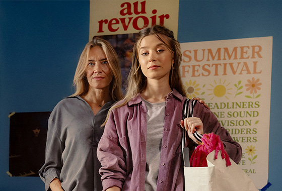 En mamma och hennes ungdom står i ett rum fullt av affischer, redo för att flytta hemifrån med en shoppingpåse i handen.