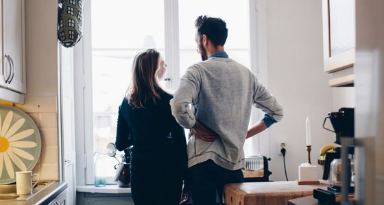 To personer st&aring;r p&aring; et lyst kj&oslash;kken og ser ut av vinduet sammen, med kaffekopper og kj&oslash;kkenutstyr rundt seg.