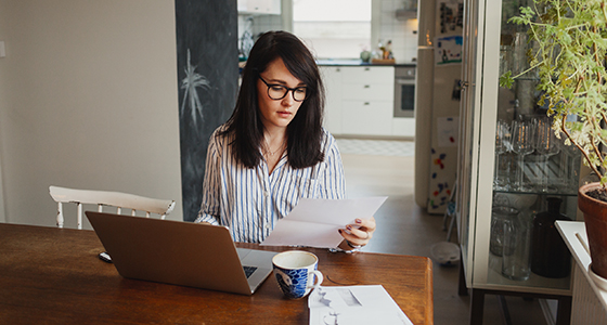 Silmälasipäinen nainen maksaa laskuja kannettavan tietokoneen ääressä