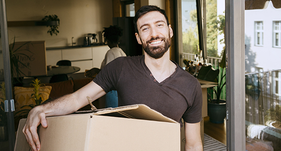 Hymyilevä partainen mies joka pitelee muuttolaatikkoa
