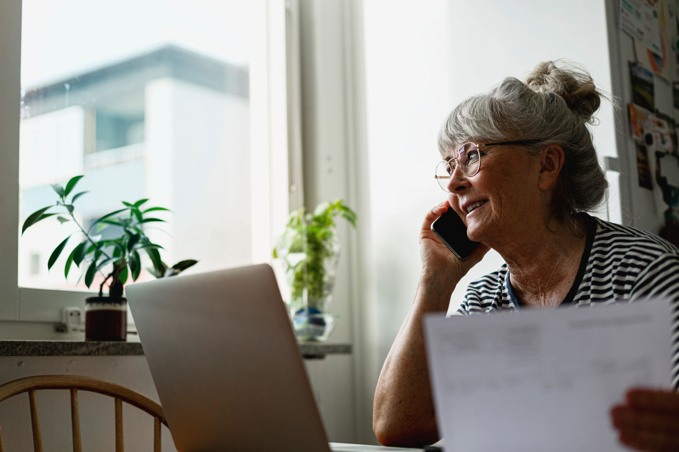 Eldre dame snakker i telefon og sitter ved PC