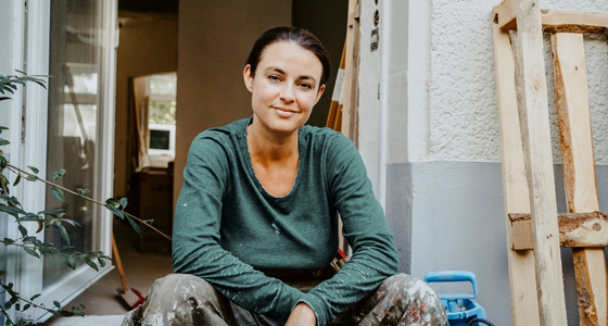 Kvinne som sitter i døråpningen under oppussing av boligen sin, et bilde som symboliserer eierskap, forbedring av hjem og økonomiske valg.