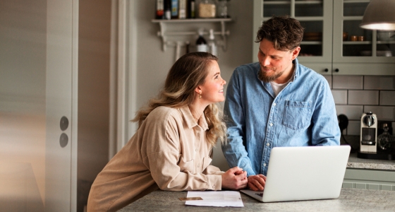 Et par som sitter sammen ved kjøkkenbenken og ser på en laptop
