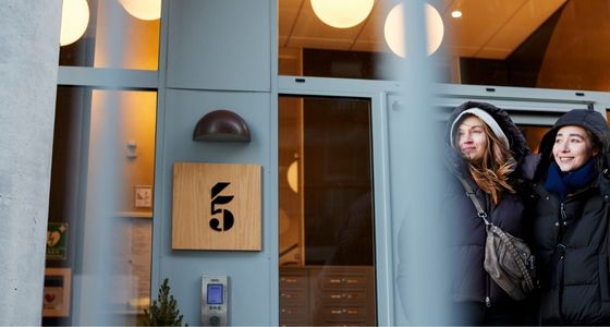 To personer st&aring;r utenfor inngangen til et moderne boligbygg i byen.