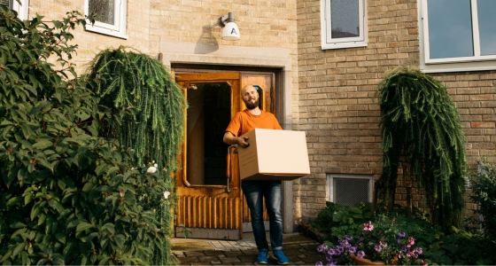 Mann står utenfor inngangsdør og bærer en flytteeske.