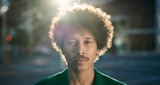 Portrett av en person som ser rett i kamera, fotografert utendørs i naturlig lys med uskarp bakgrunn.