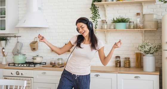 Kvinne med hodetelefoner danser p&aring; kj&oslash;kkenet mens hun h&oslash;rer p&aring; musikk.