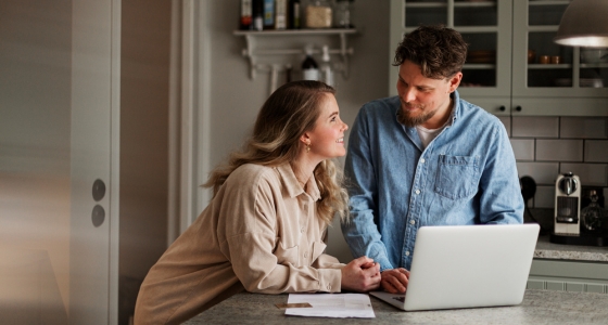 Par snakker sammen om økonomi hjemme ved kjøkkenbenken med laptop